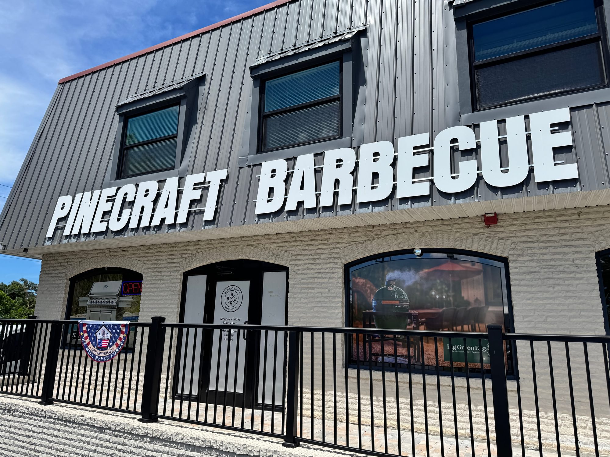 Pinecraft Barbecue storefront with large white lettering, a black railing, and a grill visible in the left window.