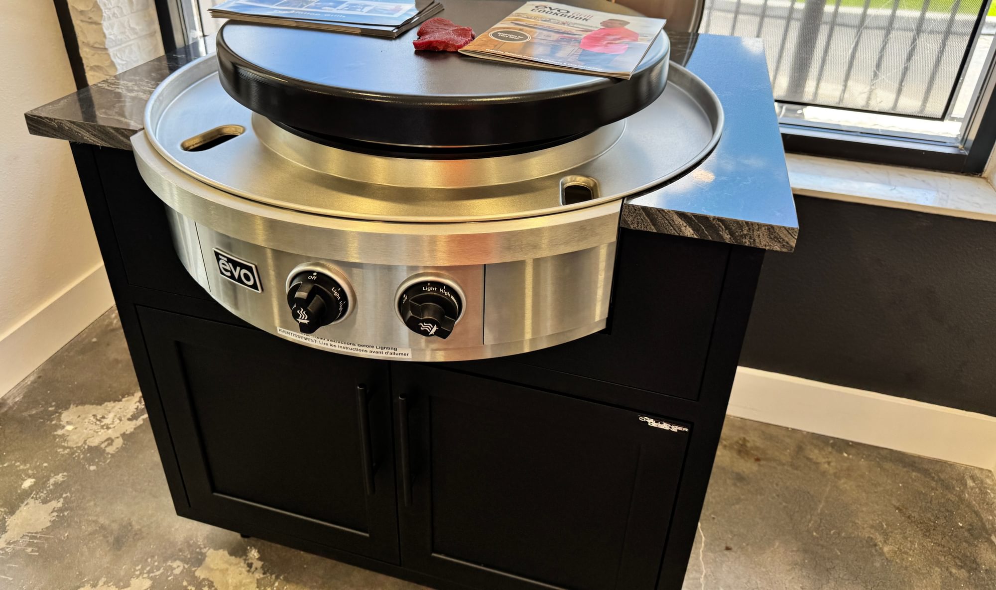 Evo round griddle on a black cabinet beside a window.
