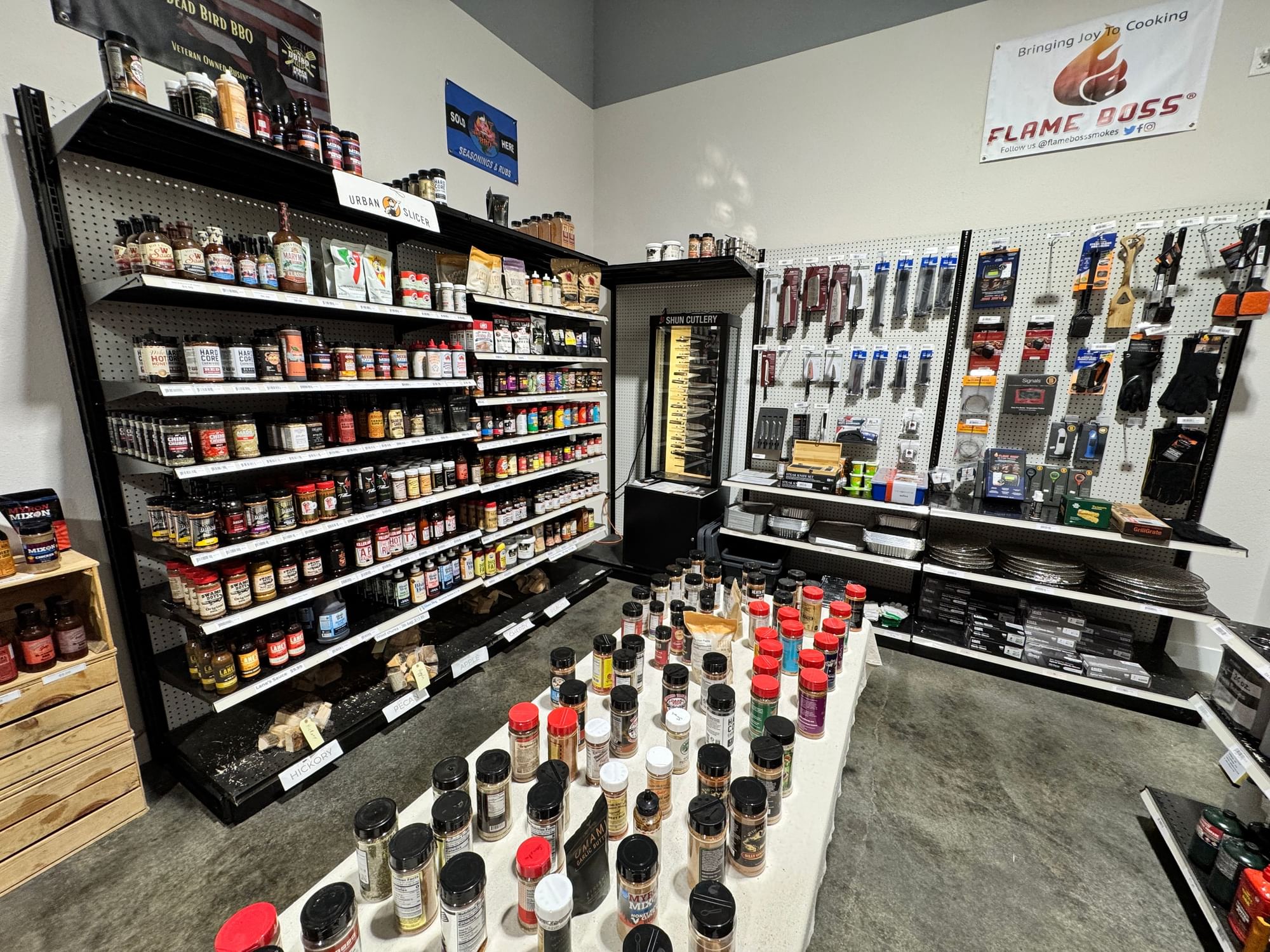 Wall of barbecue rubs and sauces with wood chunk bins in front.