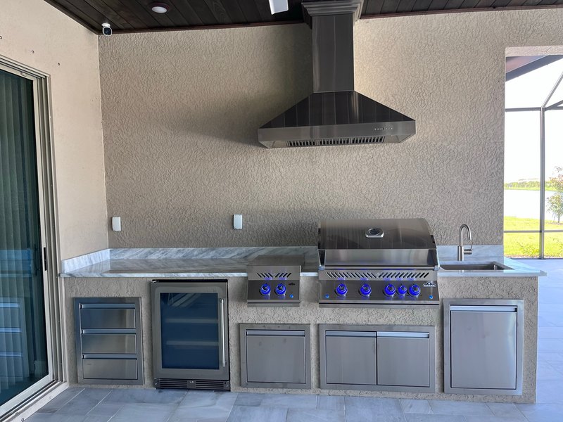 Covered outdoor kitchen with a grill, sink, and cabinets.