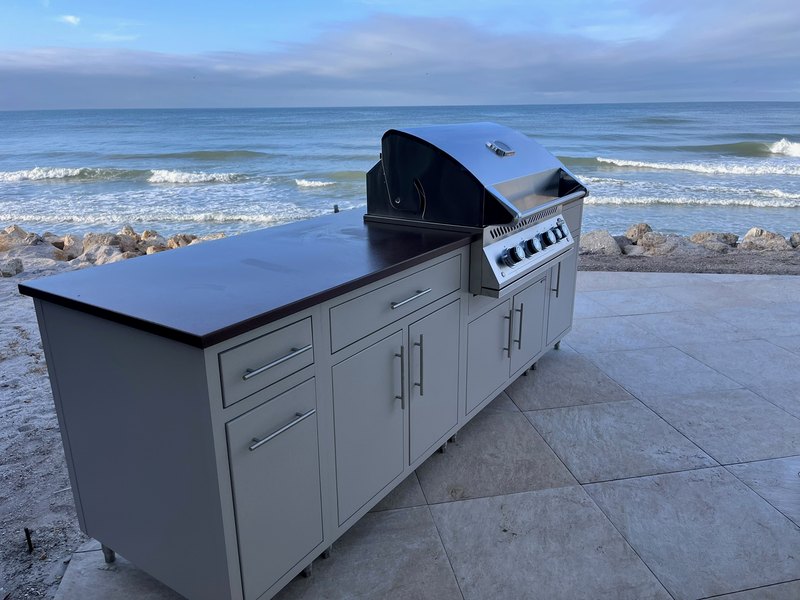 Outdoor grill island with light cabinetry beside the water.