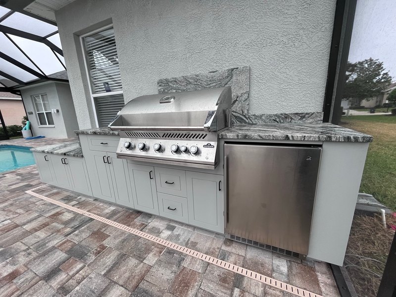 Light outdoor kitchen run with a built-in grill beside a pool.